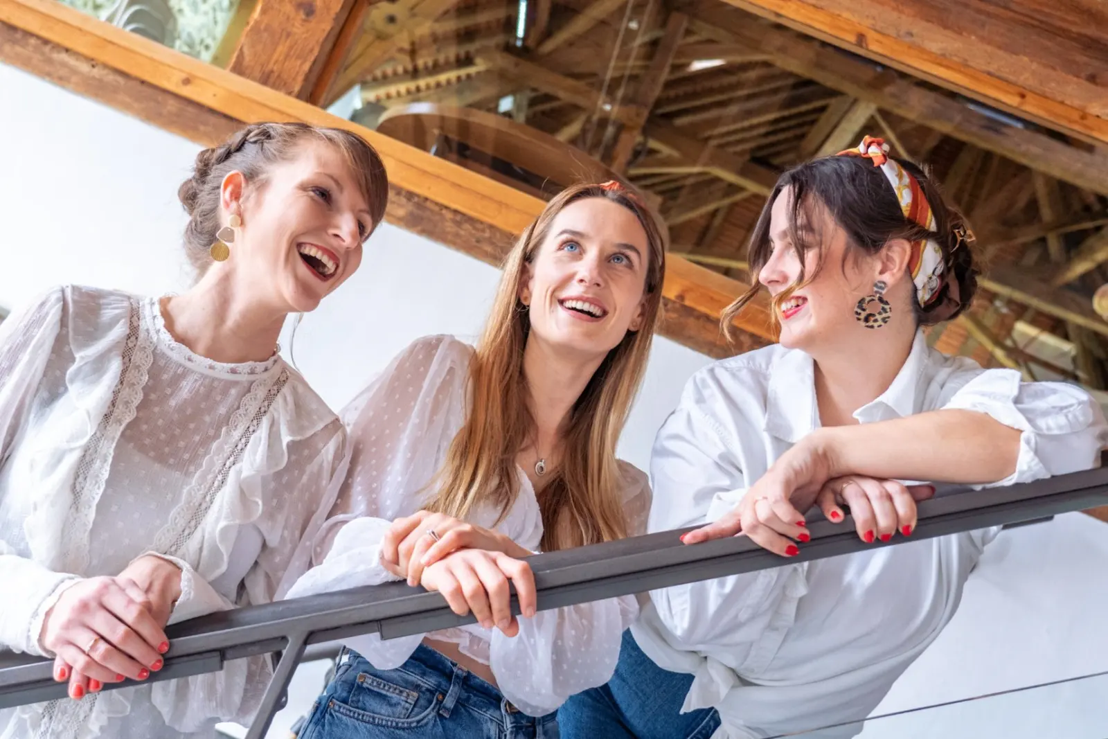 Les trois chanteuses accoudées à une balustrade, sous une charpente en bois, en train de rire