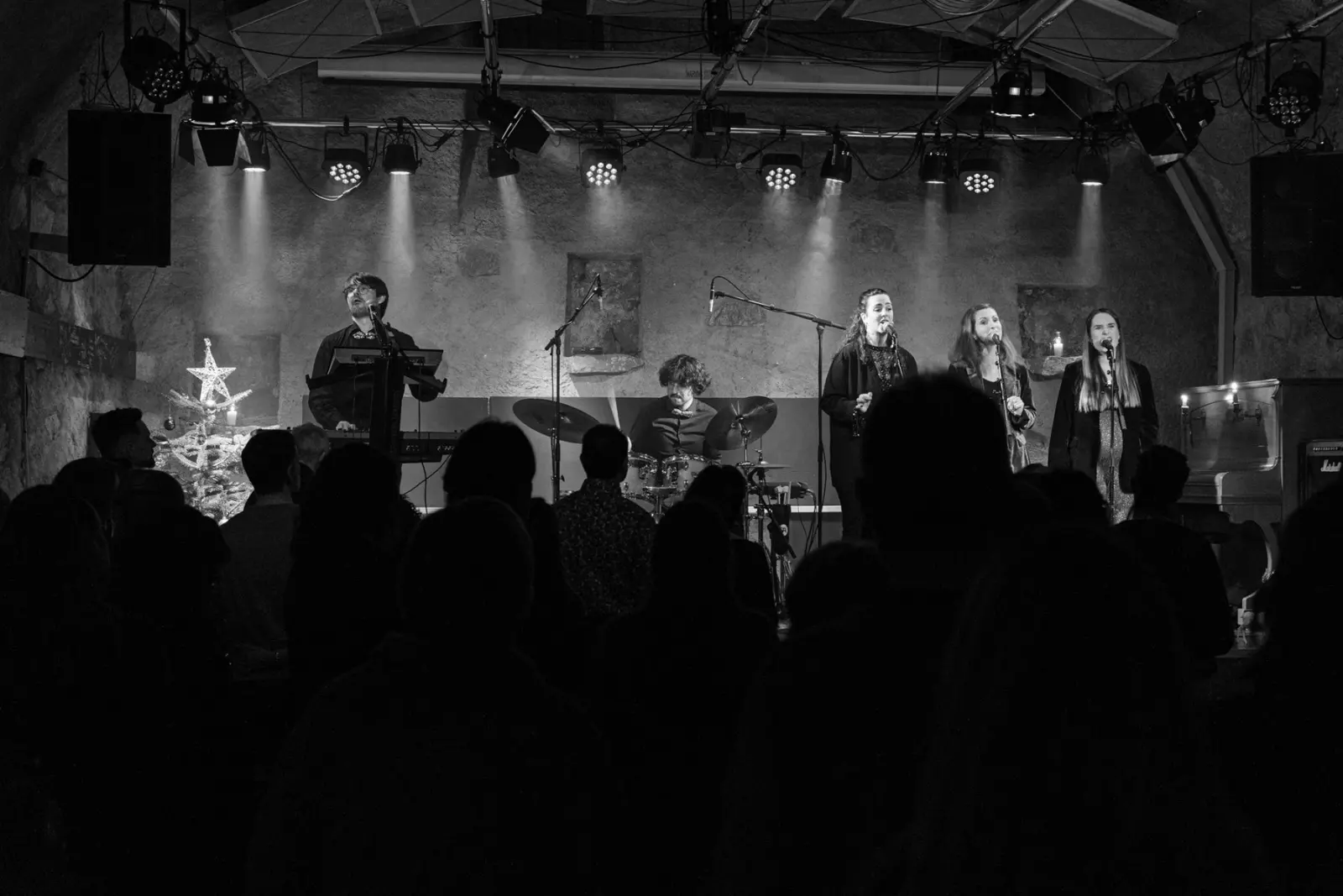 Le trio et ses musiciens sur scène, vus depuis le public, en noir et blanc