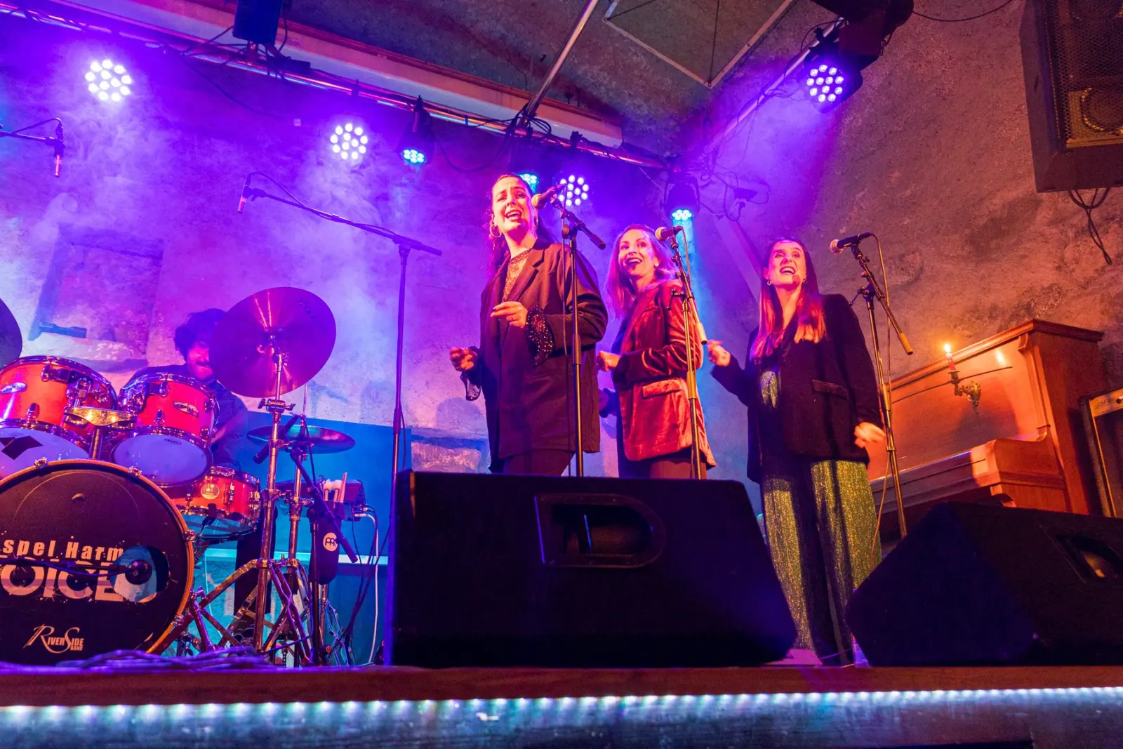 Le trio et le batteur sur scène, sous des projecteurs violets