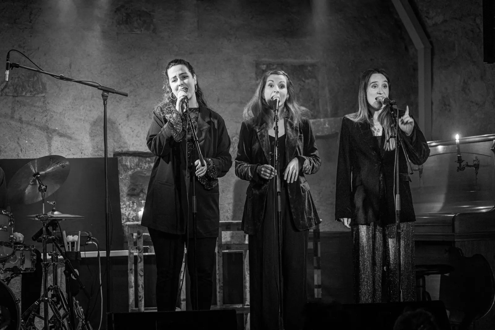 Les trois chanteuses au micro sur scène, en noir et blanc
