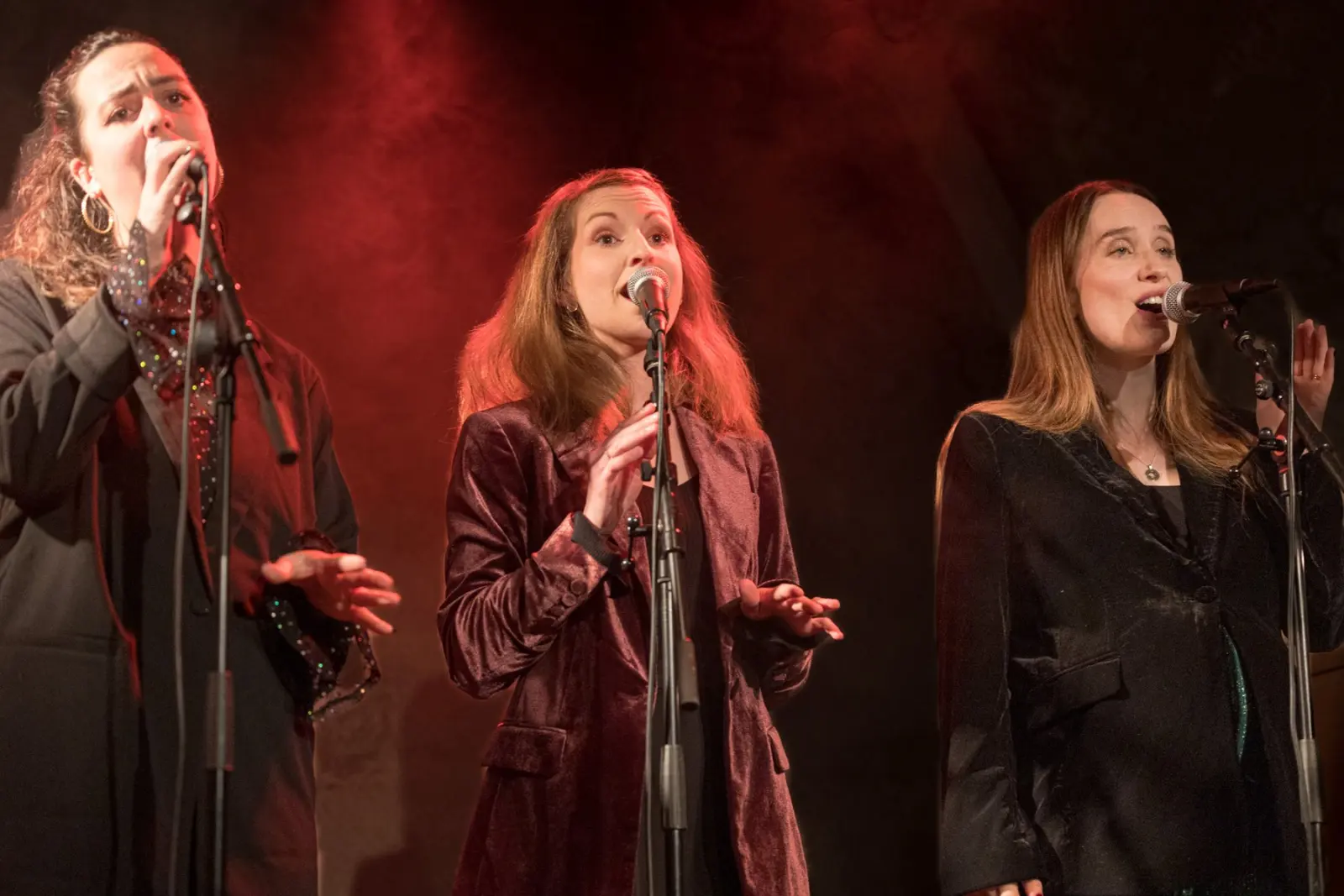 Les trois chanteuses en plein chant, dans une lumière rouge
